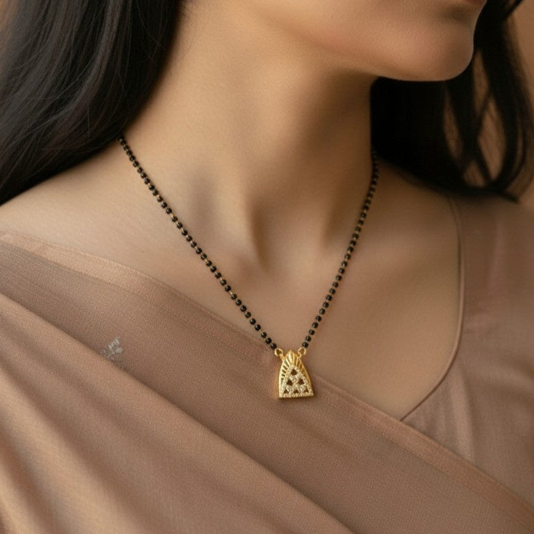 Woman wearing a gold necklace with a triangle pendant on a beige background