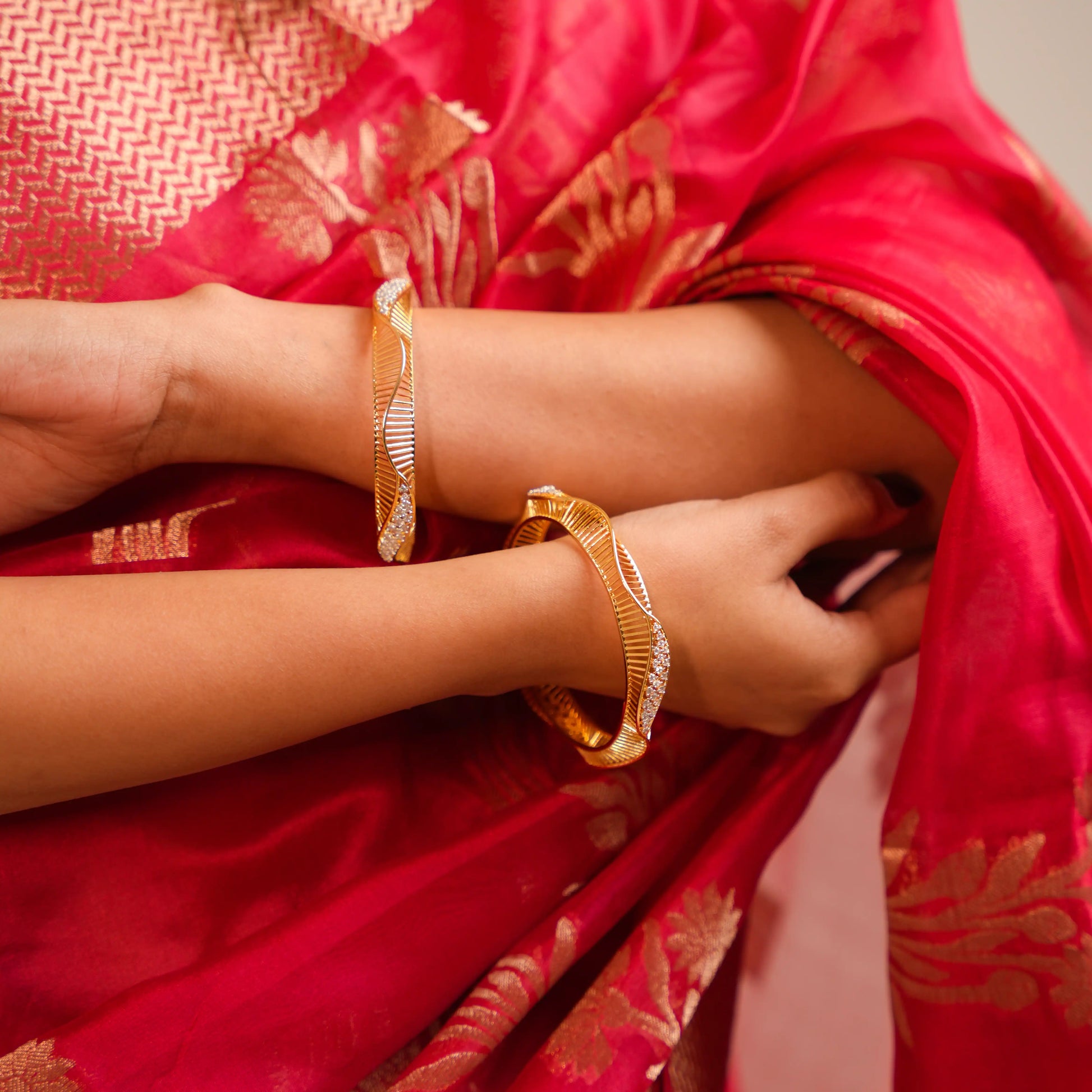 Person wearing a red saree with gold patterns and gold bangles.