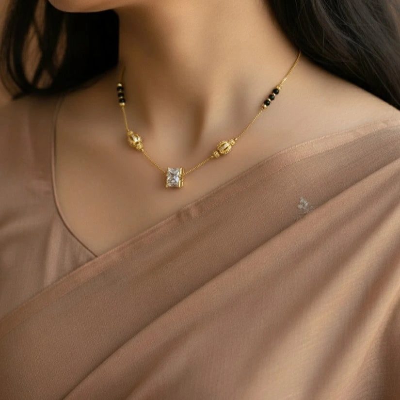 Gold necklace with a diamond pendant worn by a person in a beige garment.