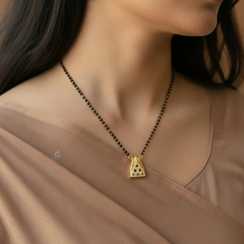 Gold necklace with a triangular pendant on a person wearing a beige top.