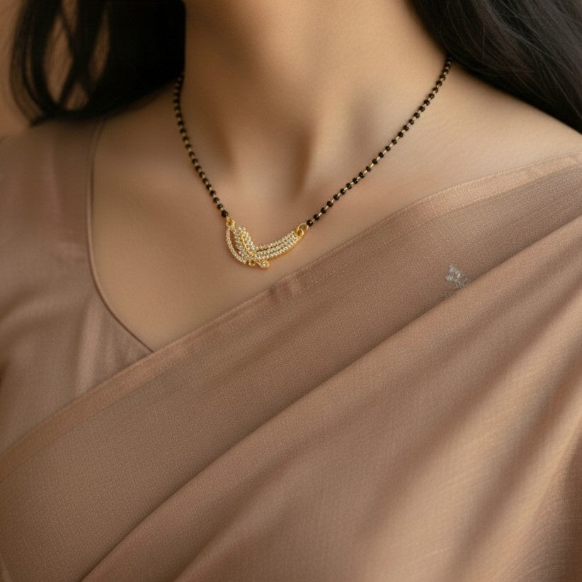 Gold necklace with a black beaded chain on a person wearing a beige saree.