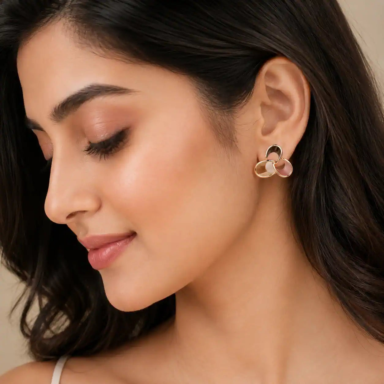 A close-up of a woman wearing a small gold-toned hoop earring with a pink floral accent, shown against her ear and dark hair. jewelry Online