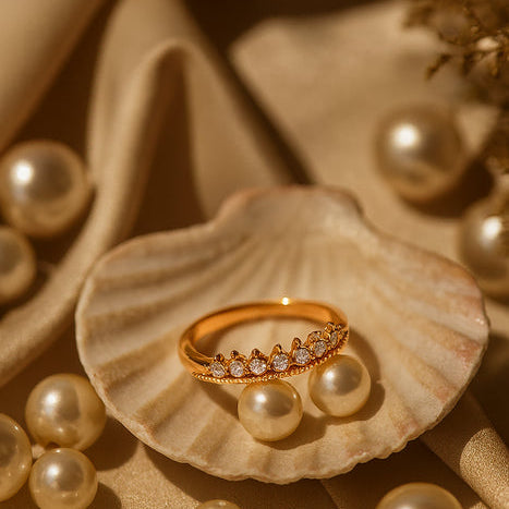 Gold ring with diamonds on a seashell surrounded by pearls on a beige fabric background