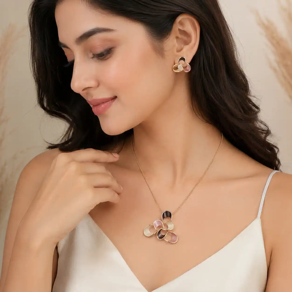 A woman wearing a delicate gold necklace and matching stud earrings with iridescent, flower-like shell or resin accents in pink, blue, and black, styled with a white satin top against a soft beige background. jewelry for white dress 
