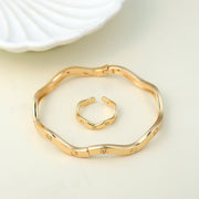 Modern gold-plated bangle and open cuff ring set featuring a sleek, wavy design with subtle embedded crystals. A perfect minimalist jewelry piece for everyday wear, office fashion, and trendy casual looks. wavy bangle bracelet, crystal-studded ring, minimalist gold jewelry, contemporary fashion accessories.