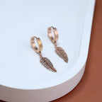 Rose gold hoop earrings with leaf-shaped pendants on a white surface.