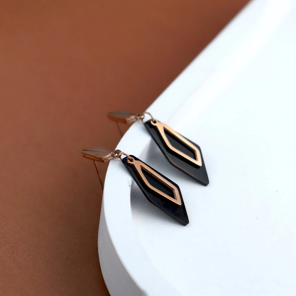 Black and rose gold earrings on a white surface with a brown background