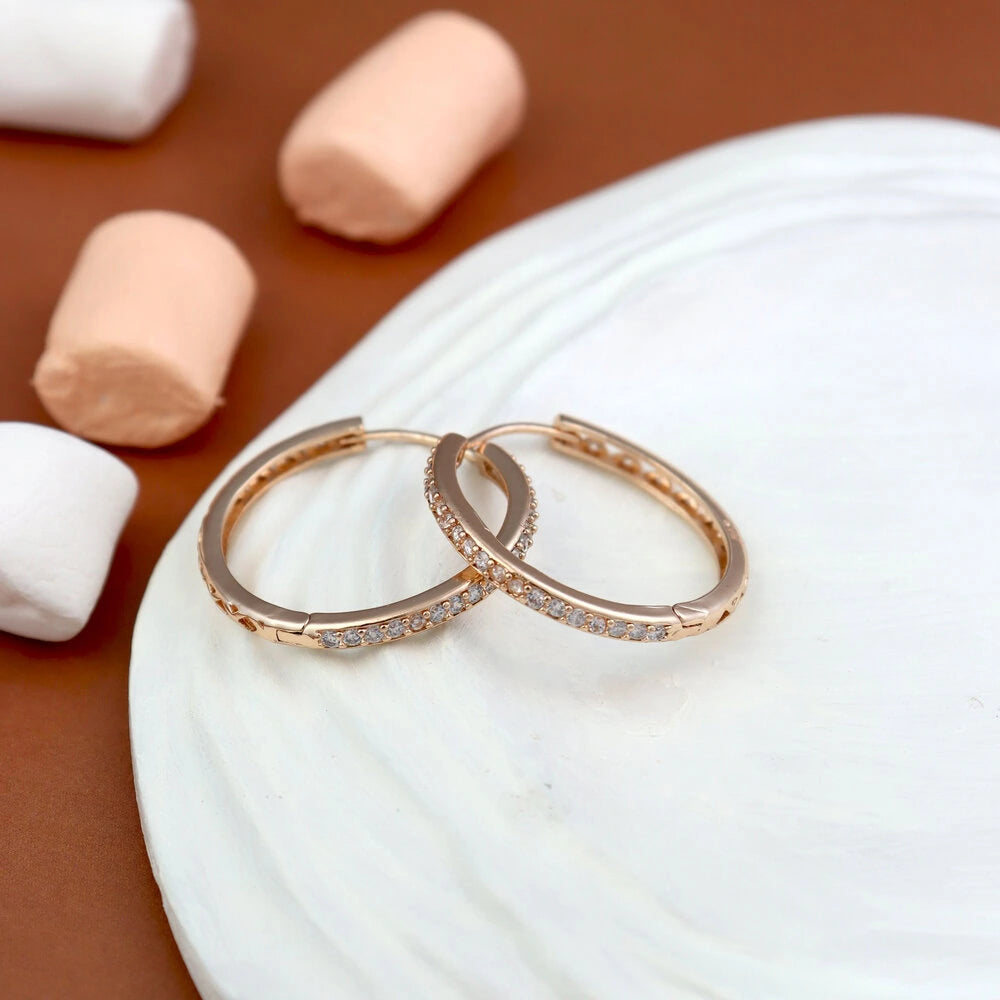 Two rose gold hoop earrings on a white shell with pink and white seashells in the background.