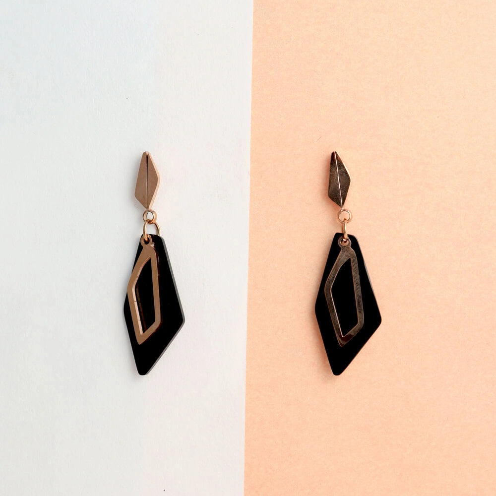 Pair of black and rose gold earrings on a two-tone background
