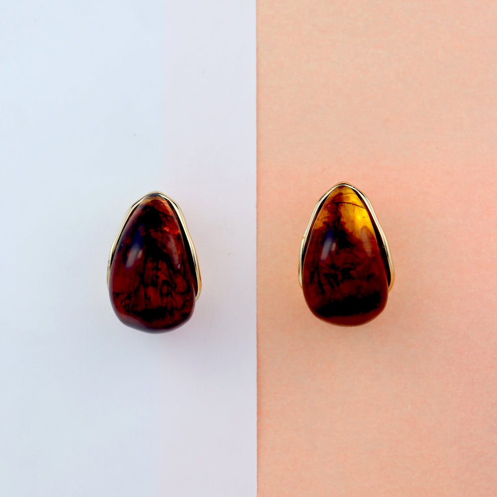 Elegant teardrop-shaped amber stud earrings with a glossy, deep brown gemstone encased in a sleek golden frame, displayed on a white tray with a warm brown background. Perfect for a classic and sophisticated look. Ideal for women’s fashion and statement jewellery collections.