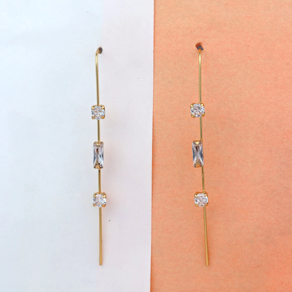 Gold earrings with clear stones on a white and peach gradient background