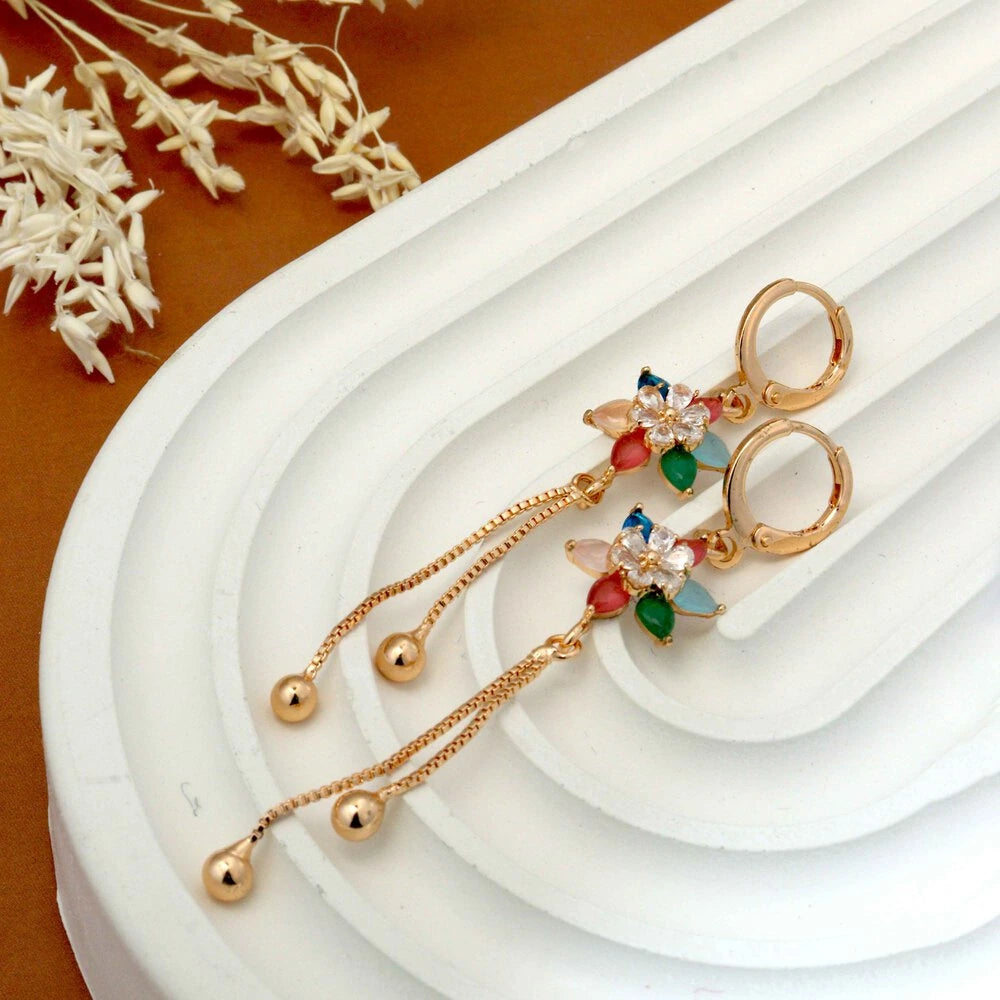 Gold earrings with colorful beads on a white stand with dried flowers in the background