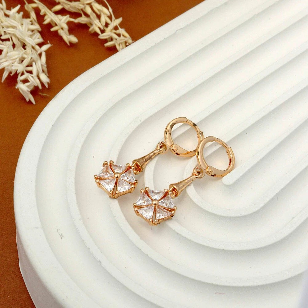 Rose gold earrings with clear gemstones on a white dish with a brown background