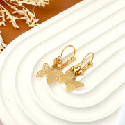Gold butterfly earrings on a white surface with a brown background