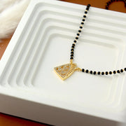 Necklace with a gold pendant on black beads on a white dish