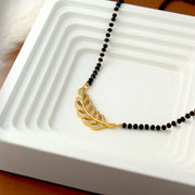 Black beaded necklace with a gold leaf pendant on a white dish