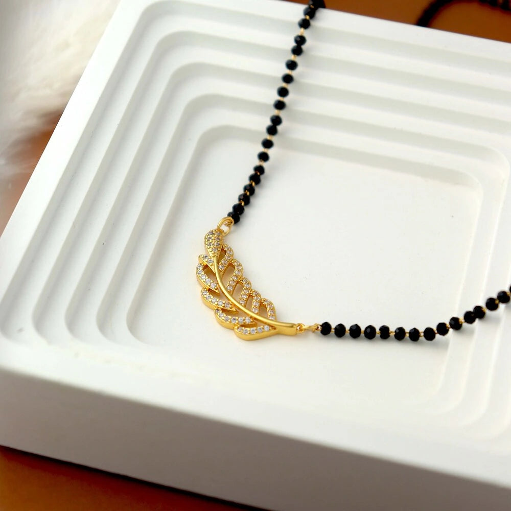 Black beaded necklace with a gold leaf pendant on a white dish