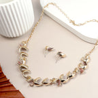Gold necklace and earrings set on a light surface with a white cup and wooden object.