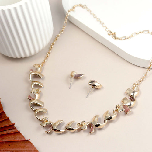 Gold necklace and earrings set on a light surface with a white cup and wooden object.