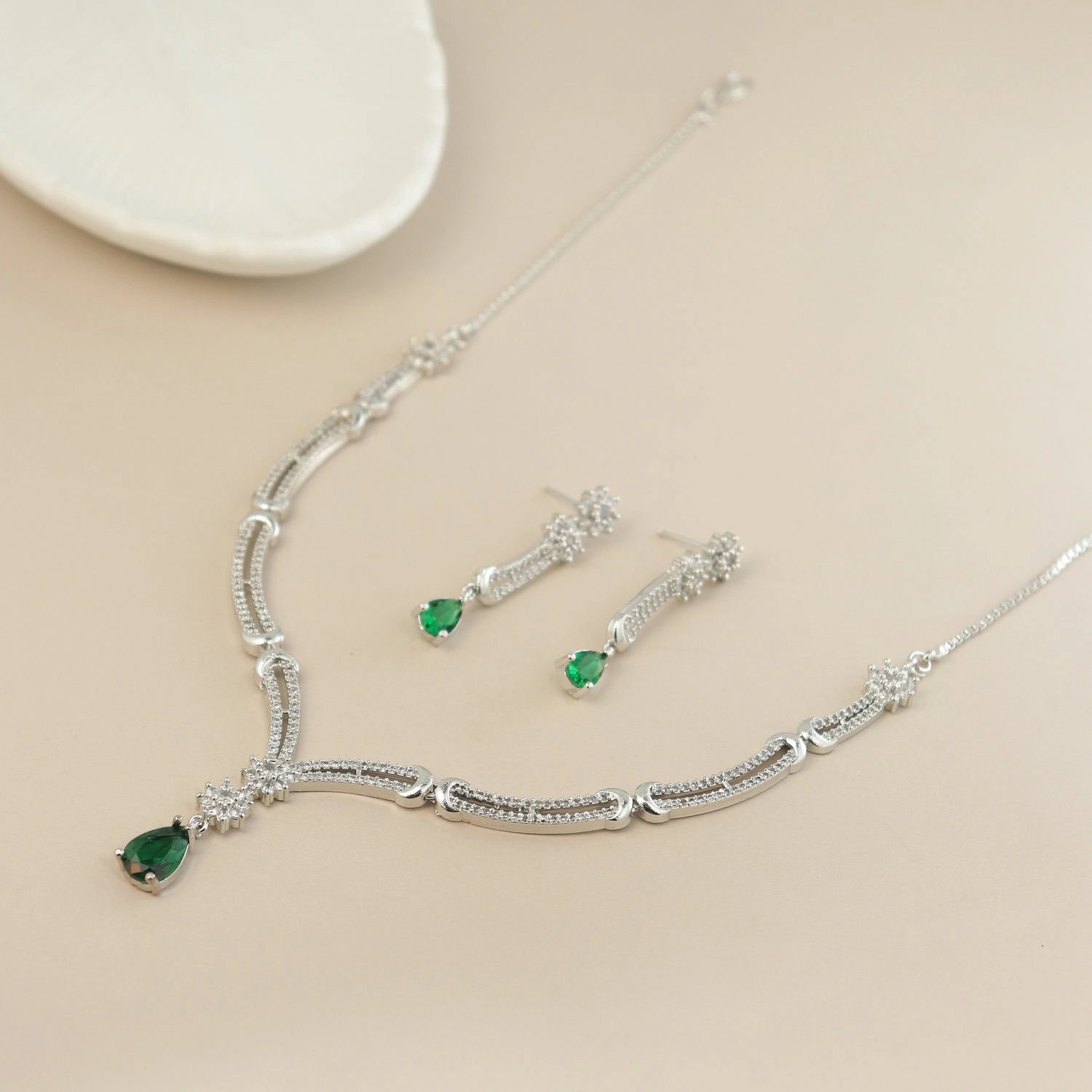 Silver necklace with emerald green gemstones on a beige surface