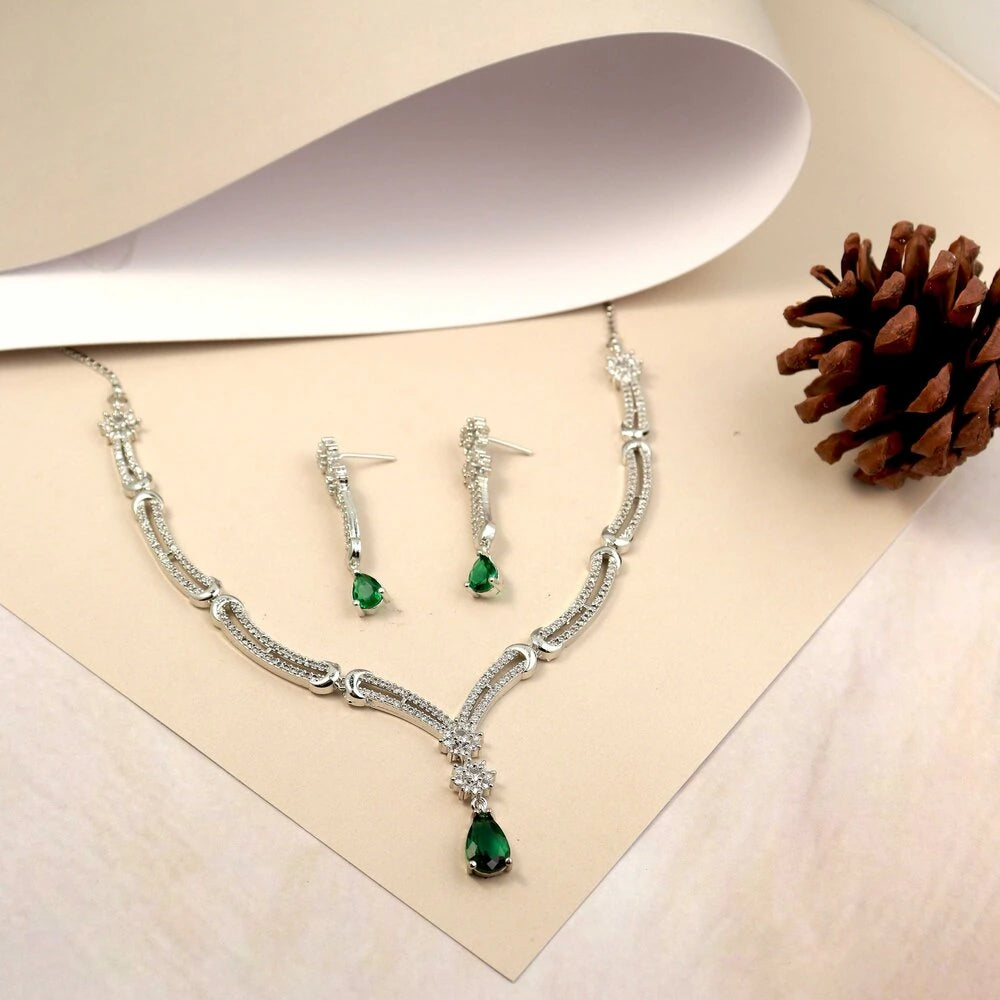 Jewelry set with necklace and earrings featuring green gemstones on a beige fabric background.