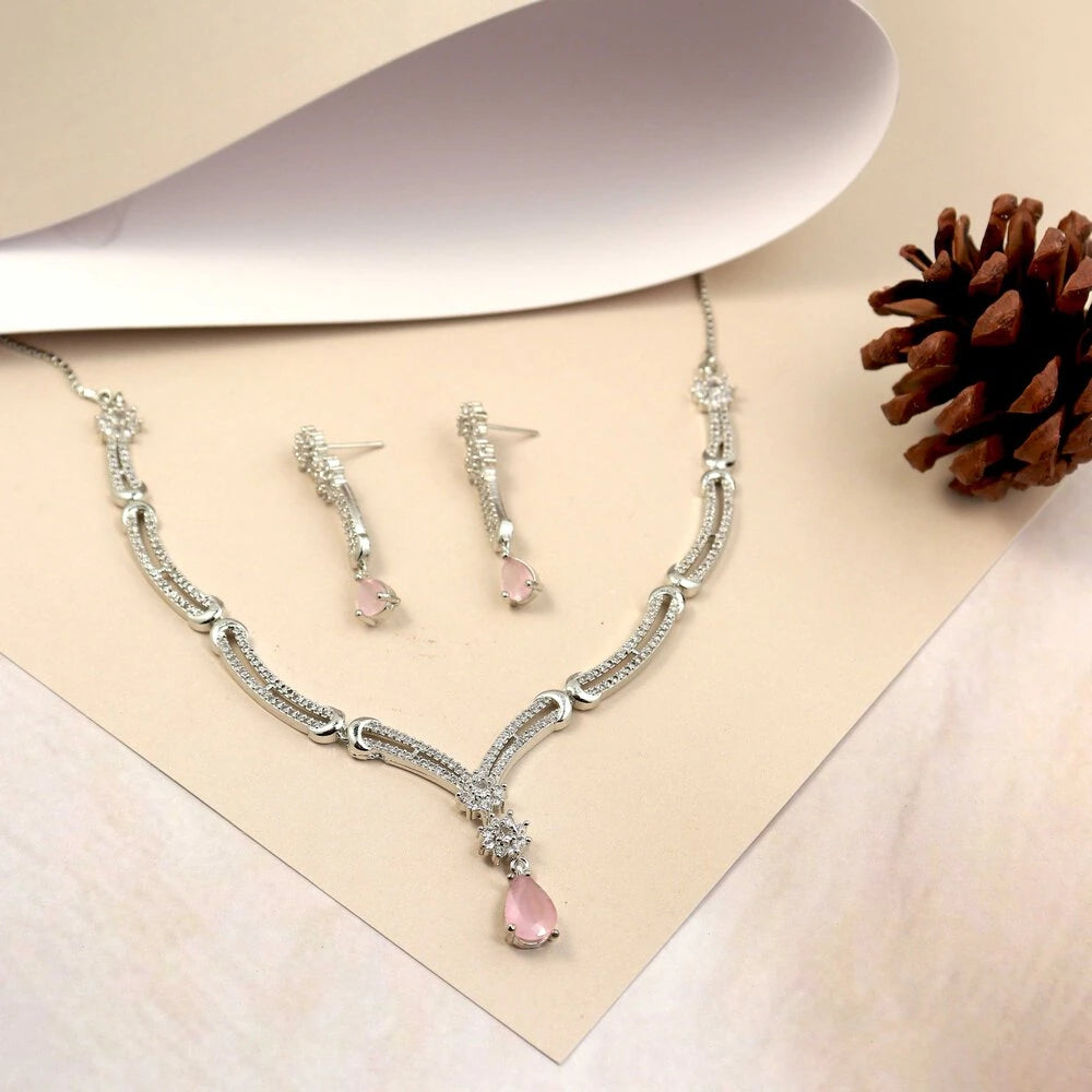 Silver necklace with pink teardrop pendant and matching earrings on a beige background