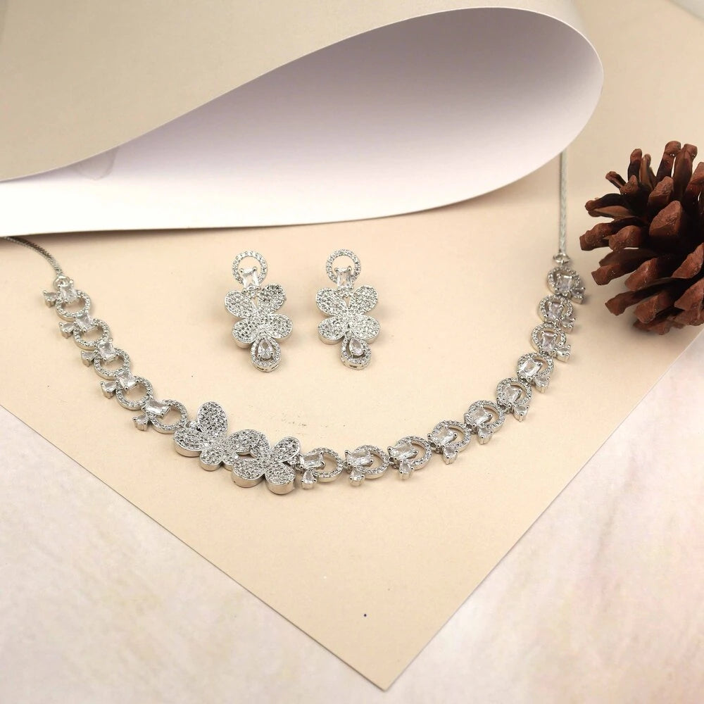 Silver necklace and earrings set on a beige background with a pine cone.