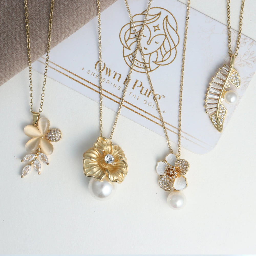 Gold necklaces with floral and leaf pendants on a white surface with 'Con Pure' branding.