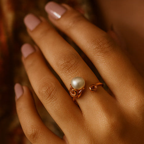 Hand wearing a gold ring with a pearl on a blurred background