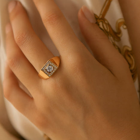 Close-up of a hand wearing a gold ring with a diamond on a soft background