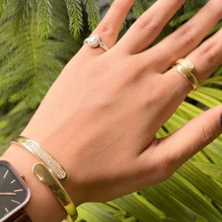 Hand wearing gold rings and a smartwatch with a green leafy background